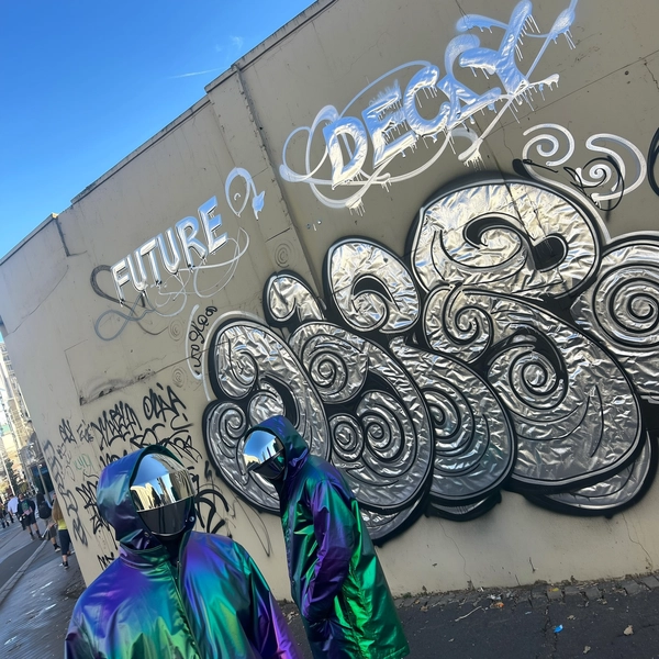 A candid urban street photo featuring a duo dressed in futuristic mirrored visors and iridescent parkas, standing casually in front of a heavily graffitied wall. The wall is adorned with prominent large chrome typography split into two lines:

"FUTURE"
"DECAY"

surrounded by intricate swirling graffiti spirals. The reflective chrome paint casts shimmering light reflections onto their iridescent parkas and visors, enhancing the futuristic vibe. Natural daylight mingles with the metallic gleam, creating authentic urban light contrasts and subtle shadows.

The textured wall shows realistic graffiti paint drips, slight weathering, and rough concrete imperfections. The composition is casually framed with a slightly tilted angle and an eye-level perspective typical of spontaneous handheld iPhone shots. The image evokes raw urban energy with genuine street authenticity and dynamic lighting, capturing both the human style and vivid vandalism culture in a documentary street photography style.