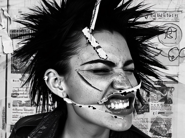 Her face fractures into anarchic layers—one eye duplicated and placed askew above the temple, the other rotated outward with a jagged paper edge. Two mouths overlap unevenly on the lower cheek, one snarling open with a torn lip, the other pressed tight, displaced near the jawline. Her nose splits diagonally, the bridge doubled and staggered, flanked by opposing ears cut with rough scissors and pasted unevenly. Collage seams peek through, masked by frayed tape strips and scattered halftone dots, invoking a hand-cut punk flyer ethos.
Her skin is gritty and raw—visible pores, sparse acne scars, and natural shine mark her pale complexion. Her spiky black hair fans out like torn paper, edges ragged and scanned with xerox grain. She wears a ripped leather jacket hinting through the tight crop, set against a grayscale background of layered newspaper textures, scribbles, and tape residues that breathe underground zine rebellion.